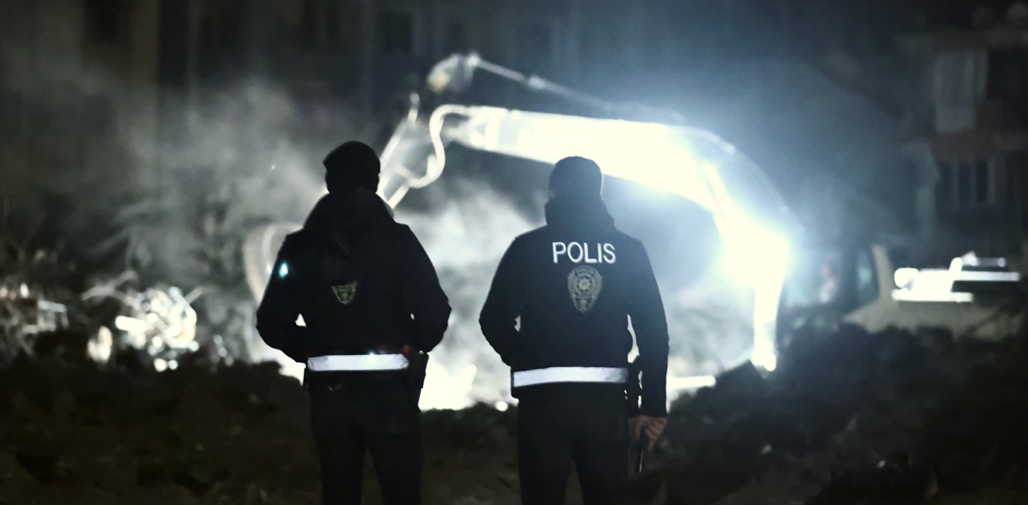 Two police officers watch process of demolishing and debris removal efforts continue in the night on collapsed buildings after earthquakes hit Turkiye.