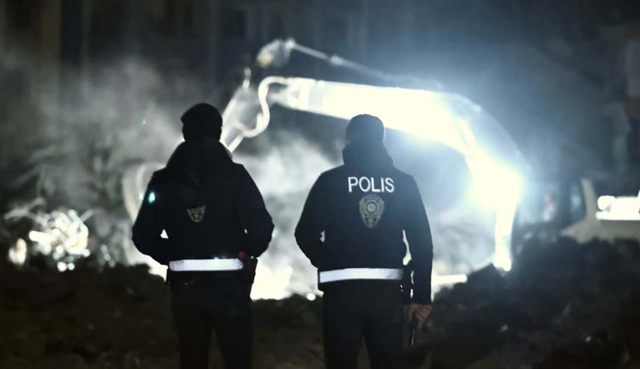 Two police officers watch process of demolishing and debris removal efforts continue in the night on collapsed buildings after earthquakes hit Turkiye.