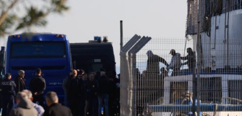 Police vans lining up, behind a fence, where police are arresting people.
